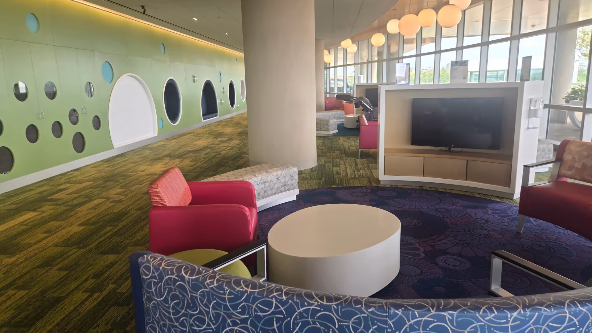 Modern interior lounge with lime-green wall panels, colorful seating, a round coffee table, and a TV.