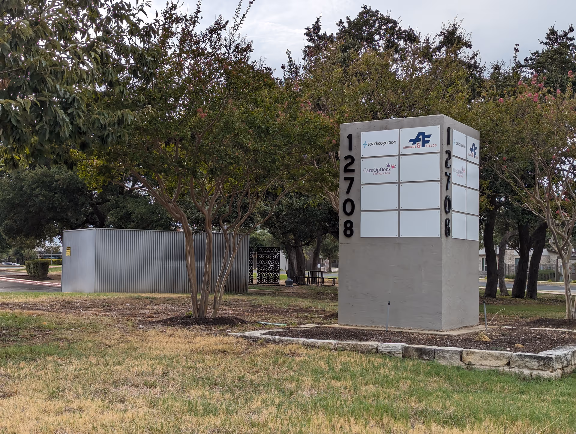 Outdoor scene with a tall directory sign showing numbers 12708 and 2708 beside trees.