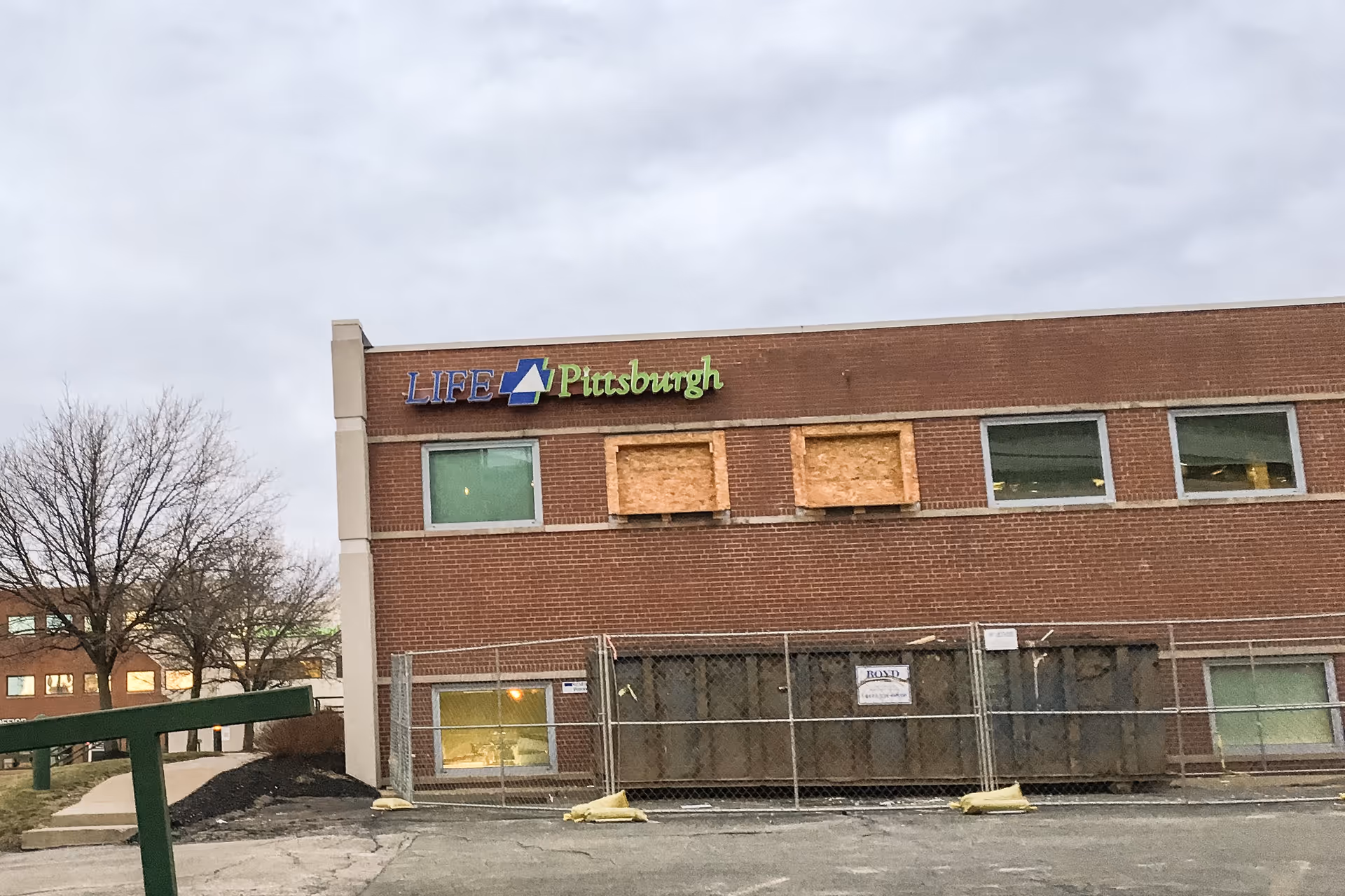 Brick building with LIFE Pittsburgh sign, boarded windows, and construction fencing.