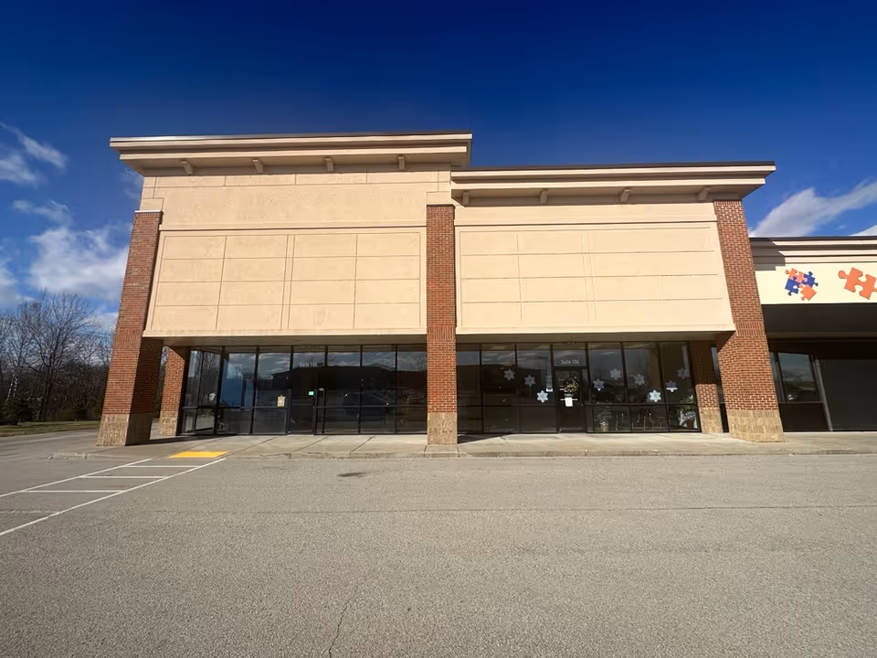 Exterior view of a beige brick building with large glass storefront doors.