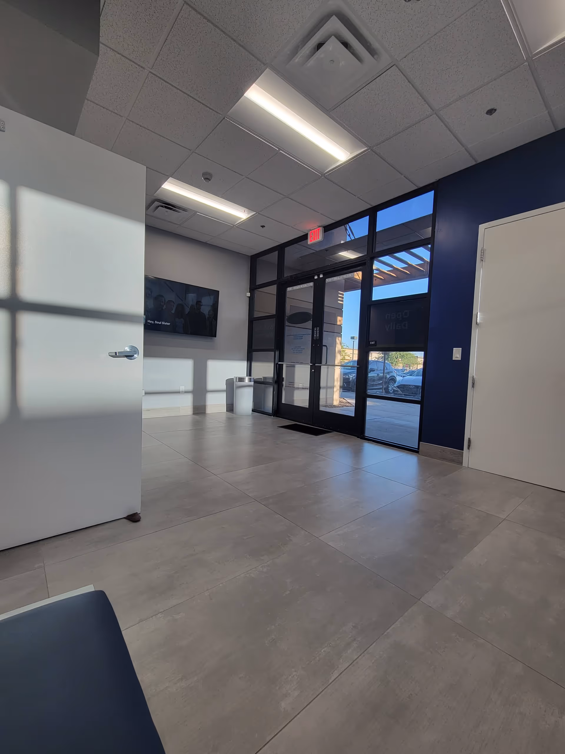 Modern facility lobby with glass doors, tiled floor, blue accent wall, and wall-mounted TV.