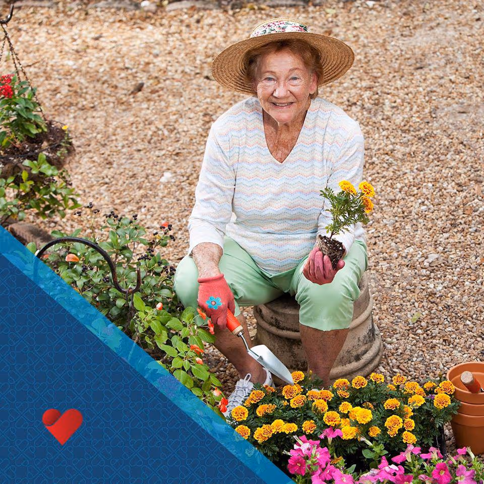 Smiling elderly woman gardening outdoors, planting yellow flowers in a gravel yard.