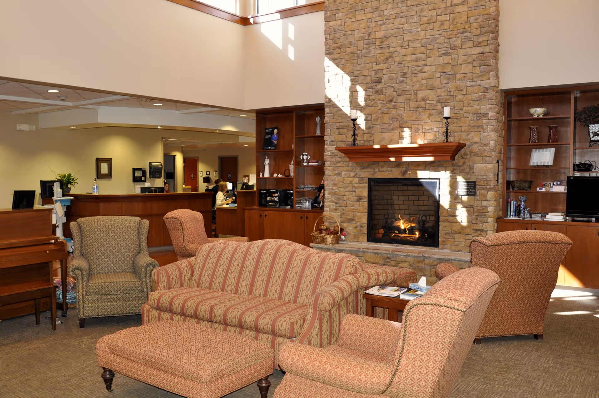 Cozy senior living lounge with a stone fireplace, comfortable seating, and a reception desk.