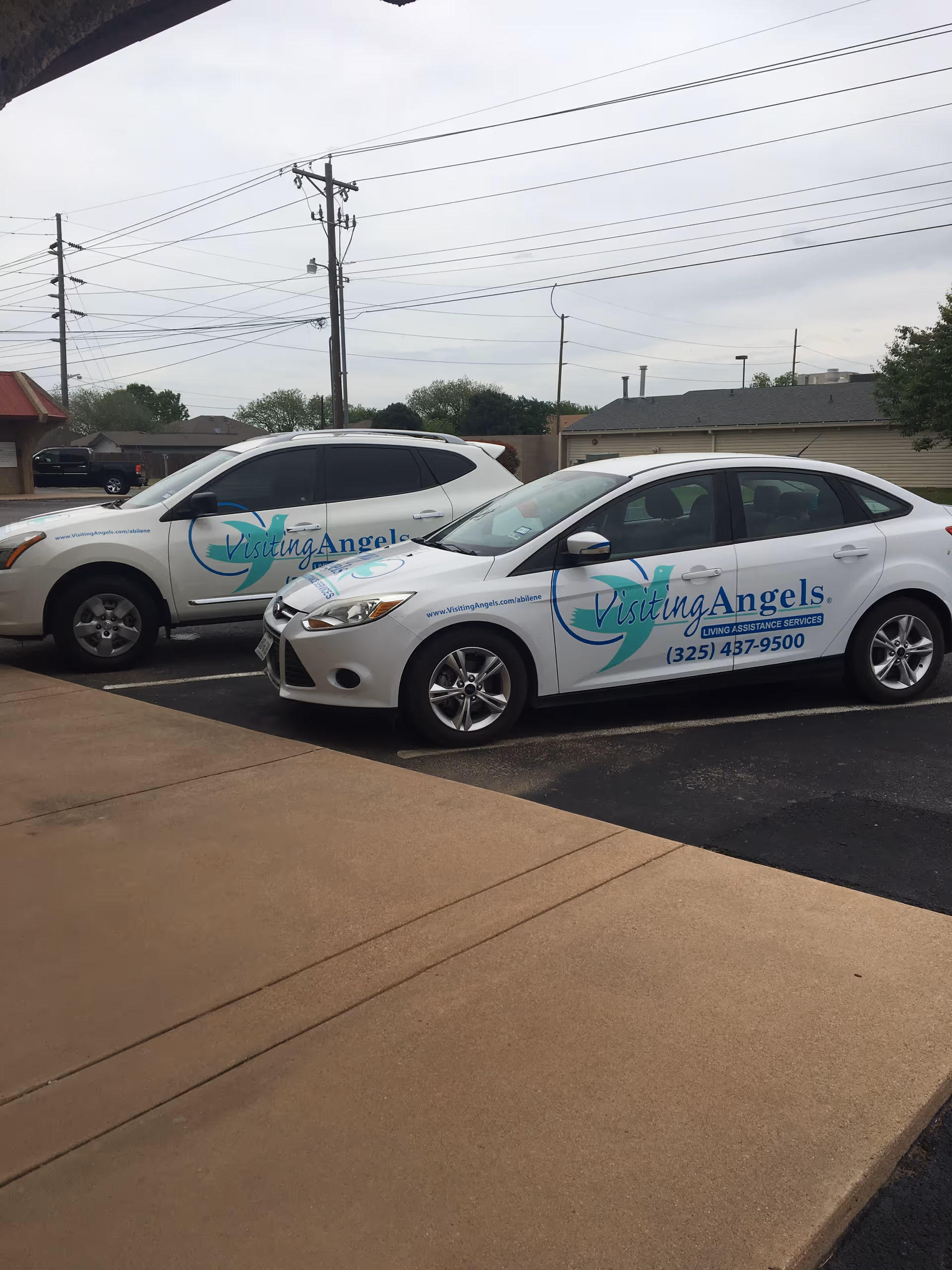 Two white Visiting Angels vans parked in a driveway with power lines overhead