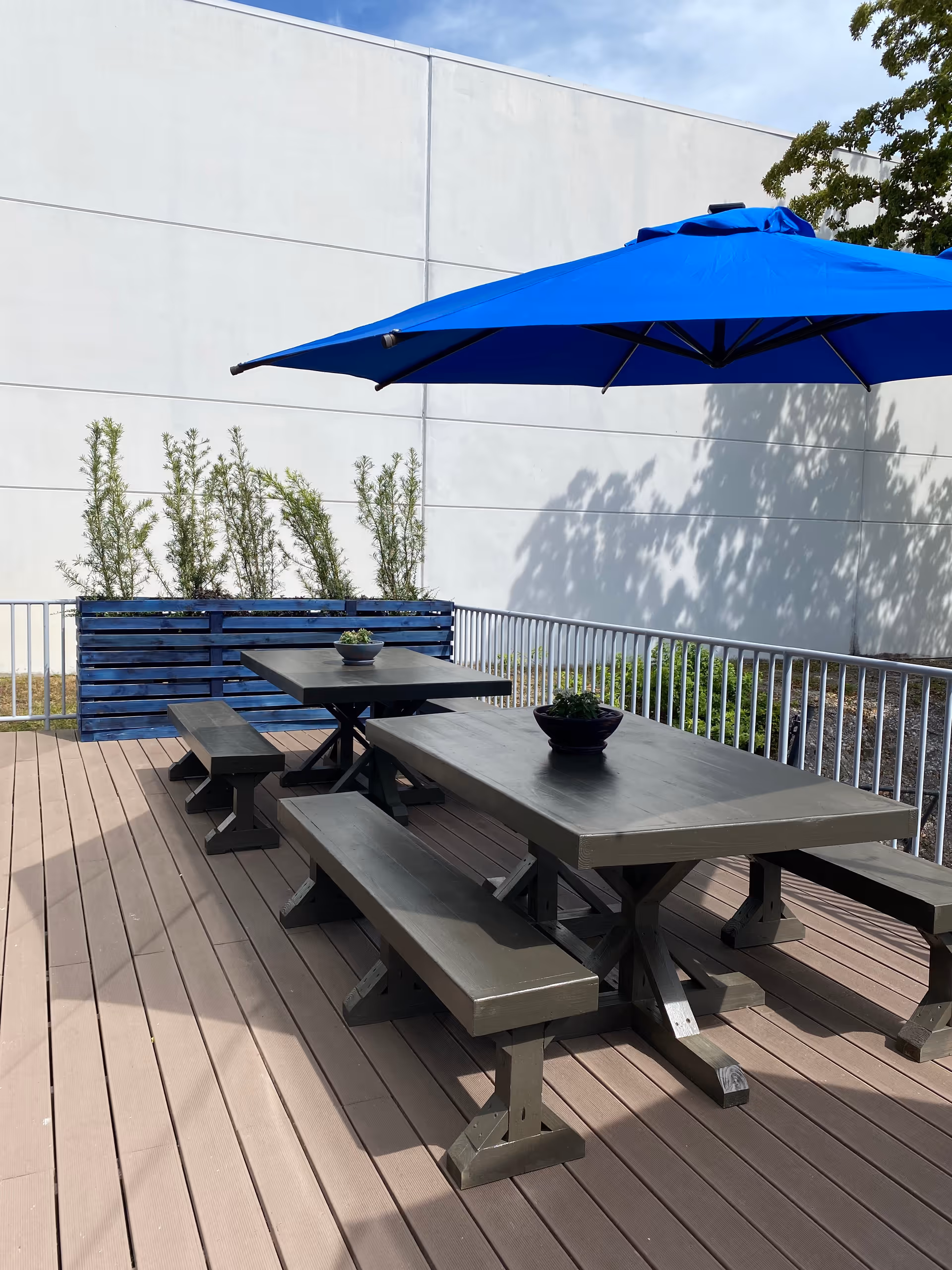 Outdoor wooden patio with picnic tables and a blue umbrella.