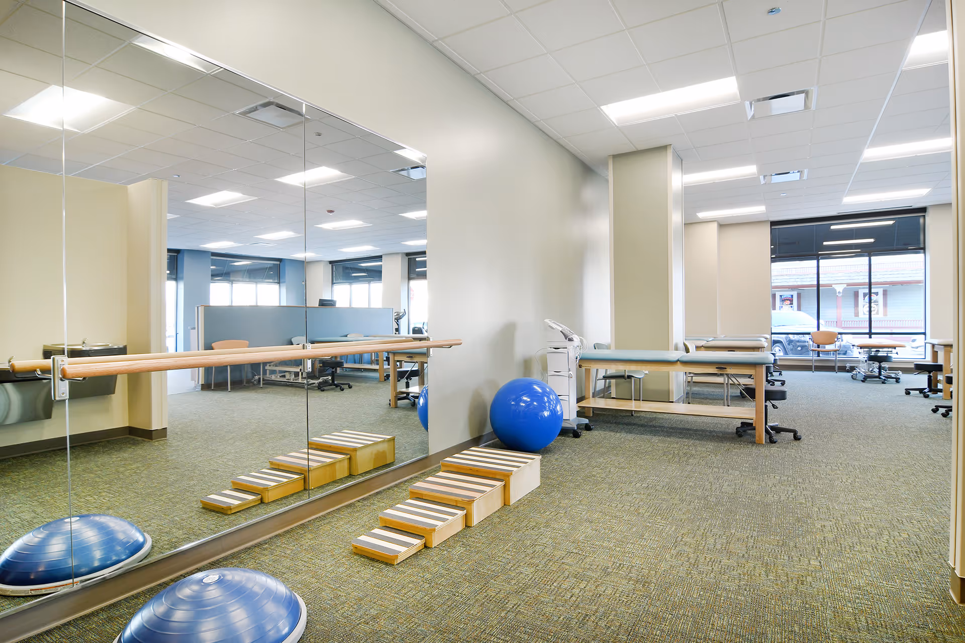 Interior of a physical therapy space with mirrors, a barre, exercise equipment, and treatment tables.