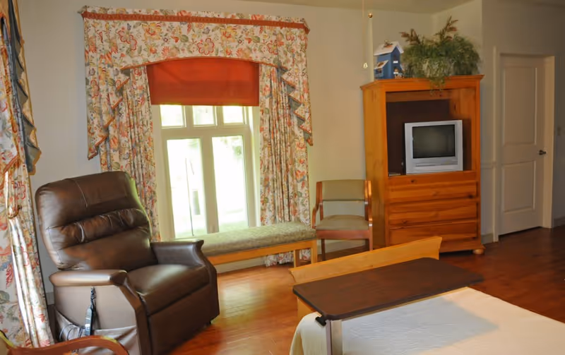 Cozy living room with leather chair, window seat, floral curtains, and wooden furniture.