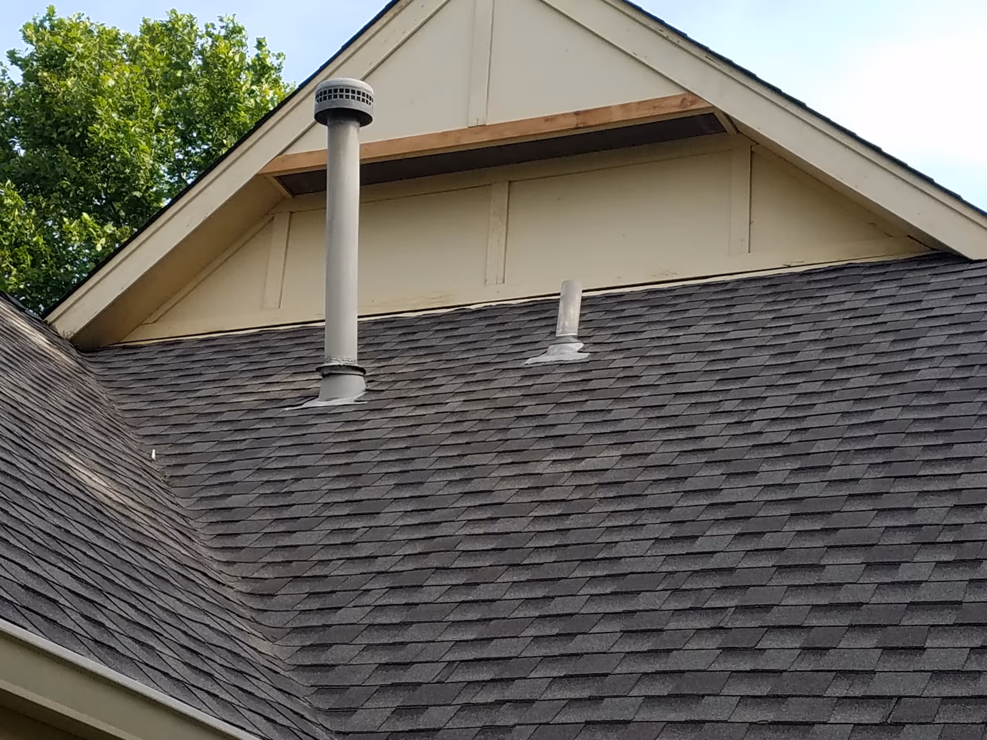 Close up of a sloped shingled roof with metal vents on a light exterior.
