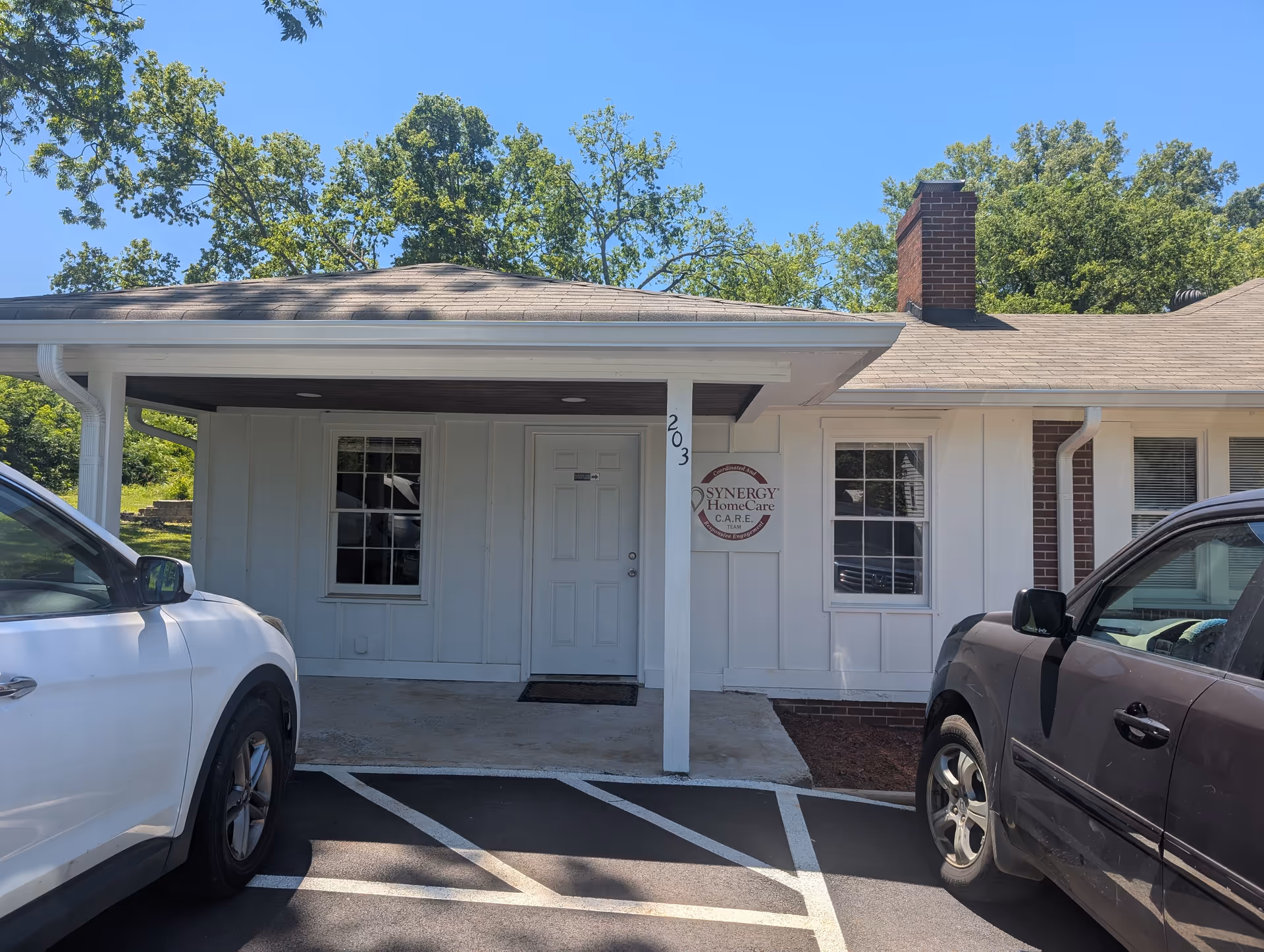 Front view of a single-story building entrance with Synergy HomeCare sign and parked cars.