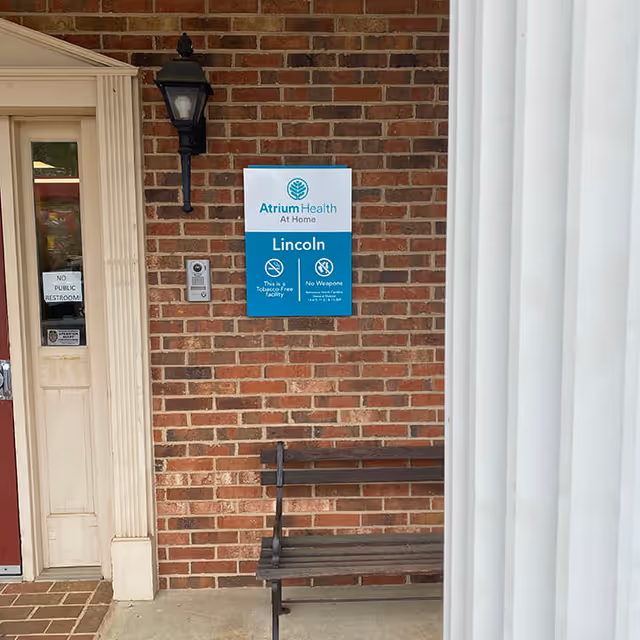Exterior brick entrance with a bench and Atrium Health At Home sign.