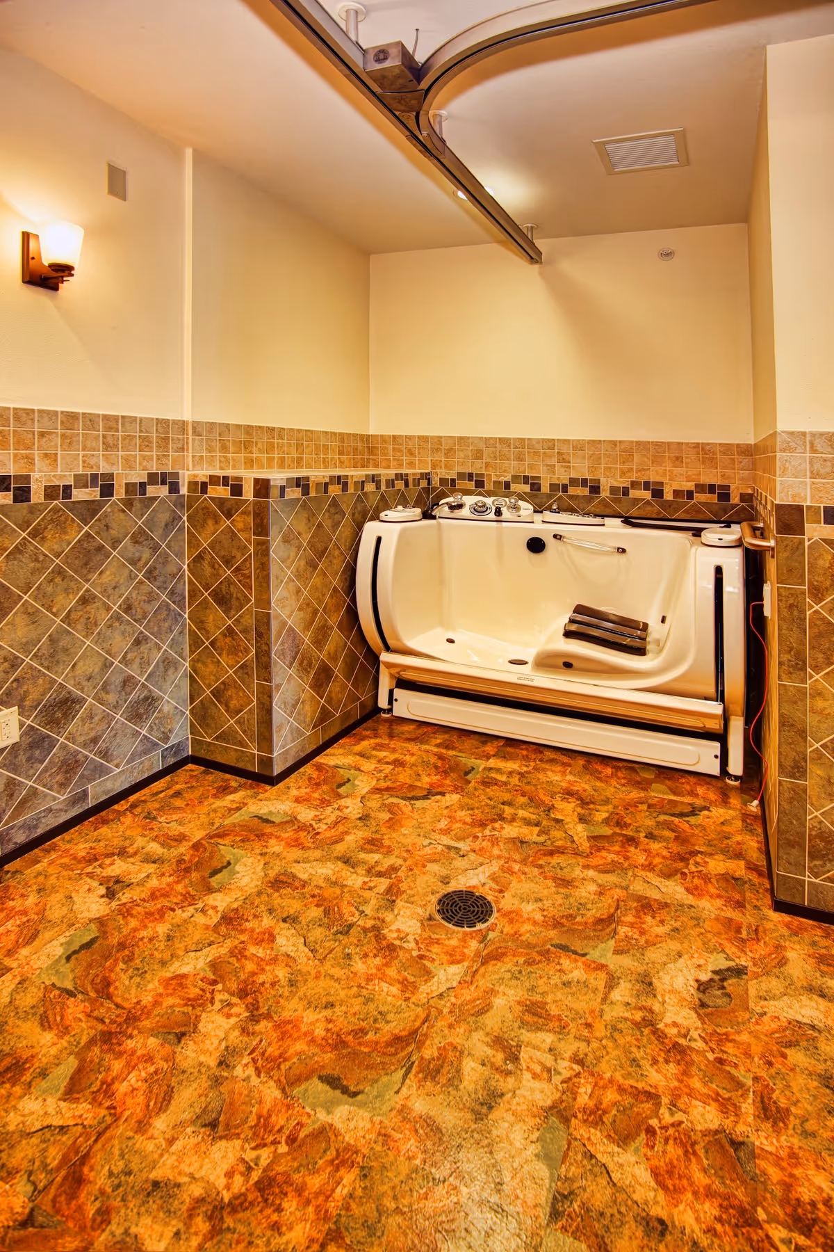 Accessible whirlpool bathtub against tiled walls in a warm, empty facility bathroom.