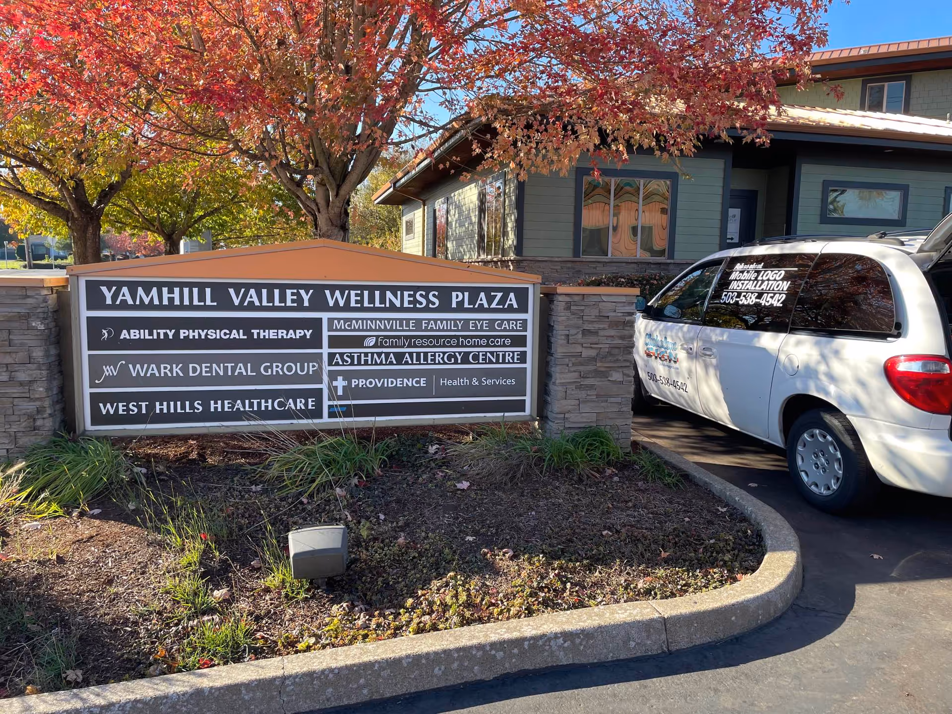 Exterior view of Yamhill Valley Wellness Plaza sign with a white van parked nearby.