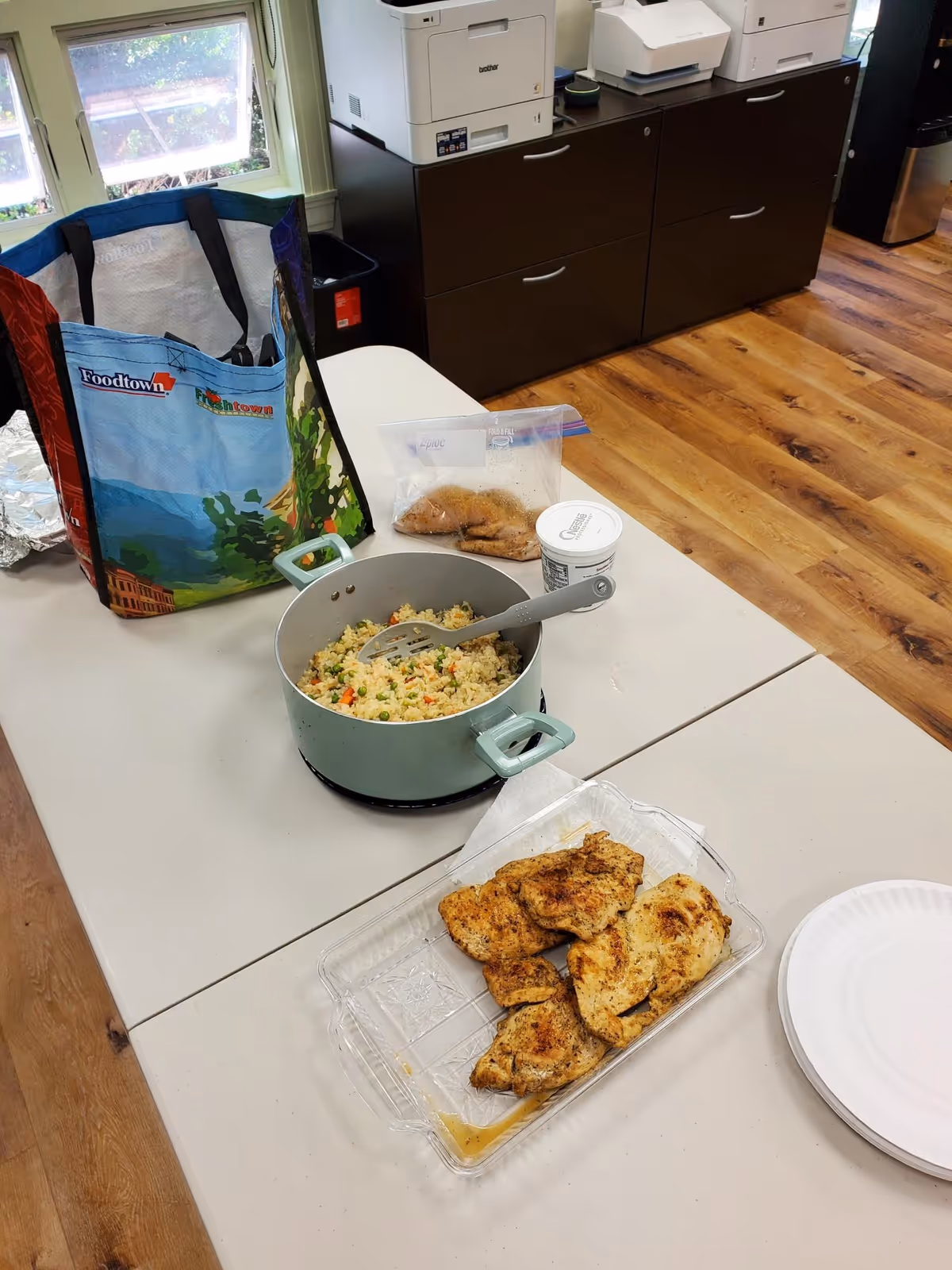 Table with pot of fried rice, breaded chicken, plastic containers, and printers in an indoor room.