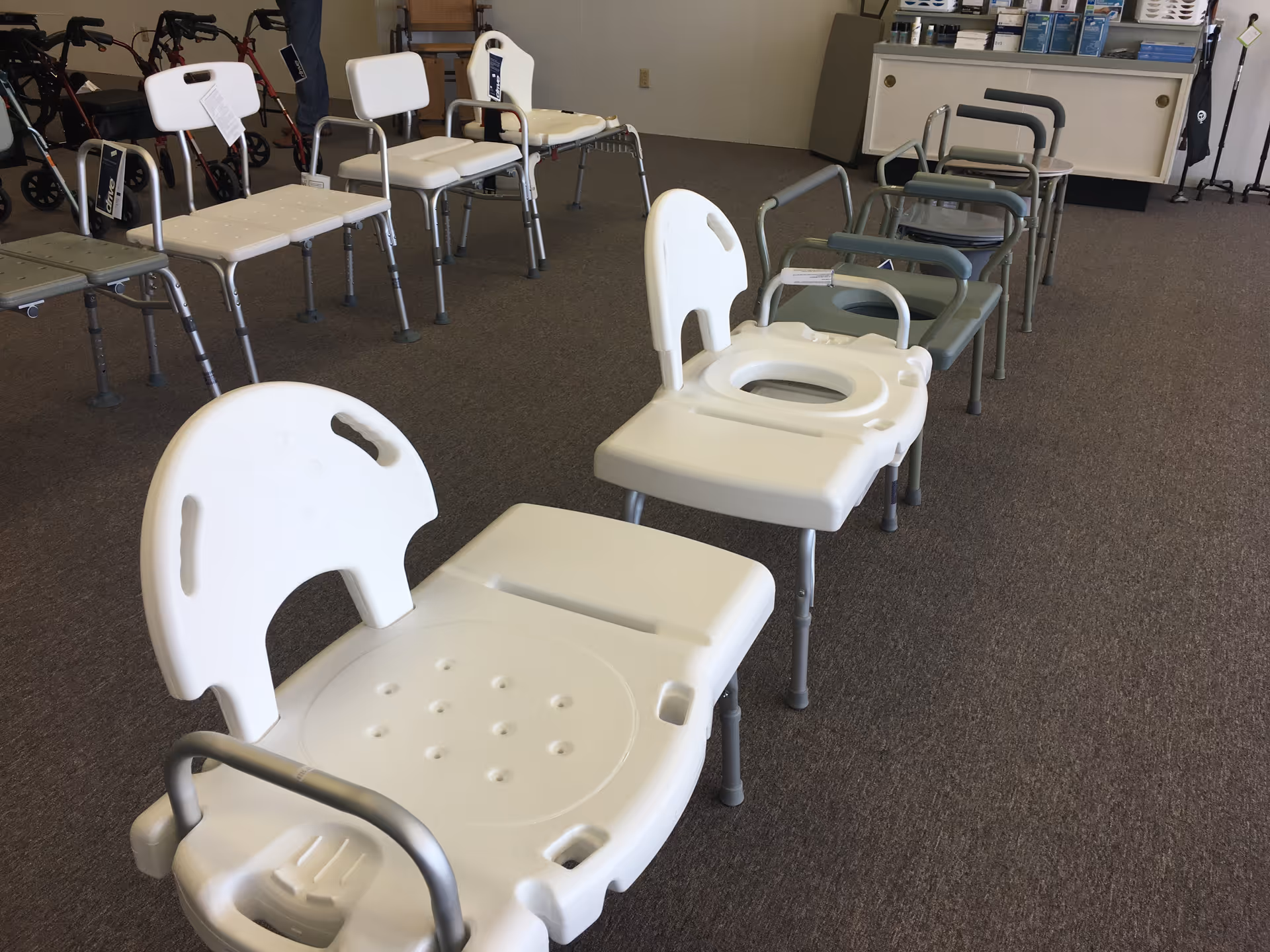 Row of white bathroom chairs arranged in a showroom with medical supplies in background.