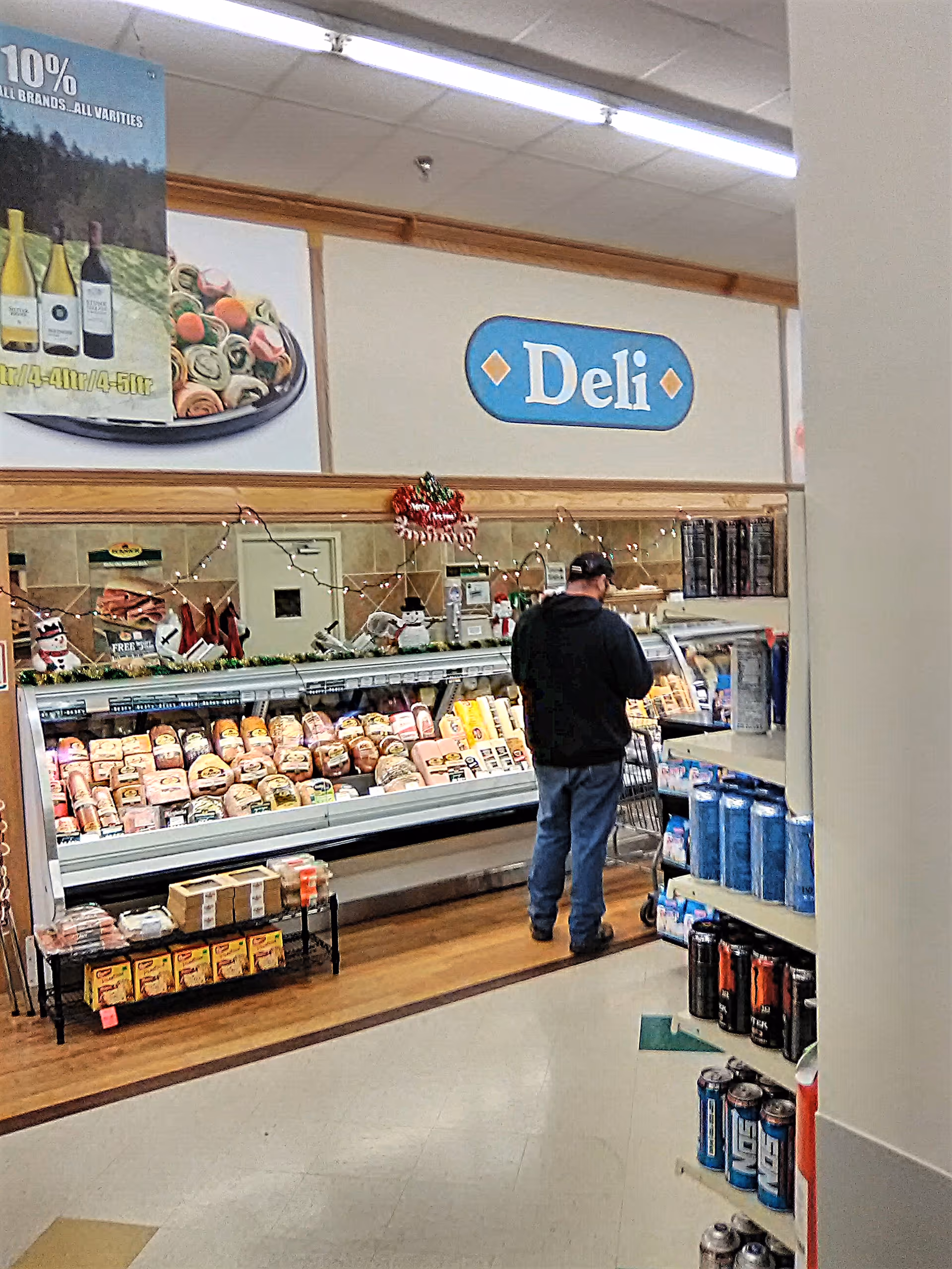 A man in a dark hoodie browses the deli counter inside Discount Drug Mart.