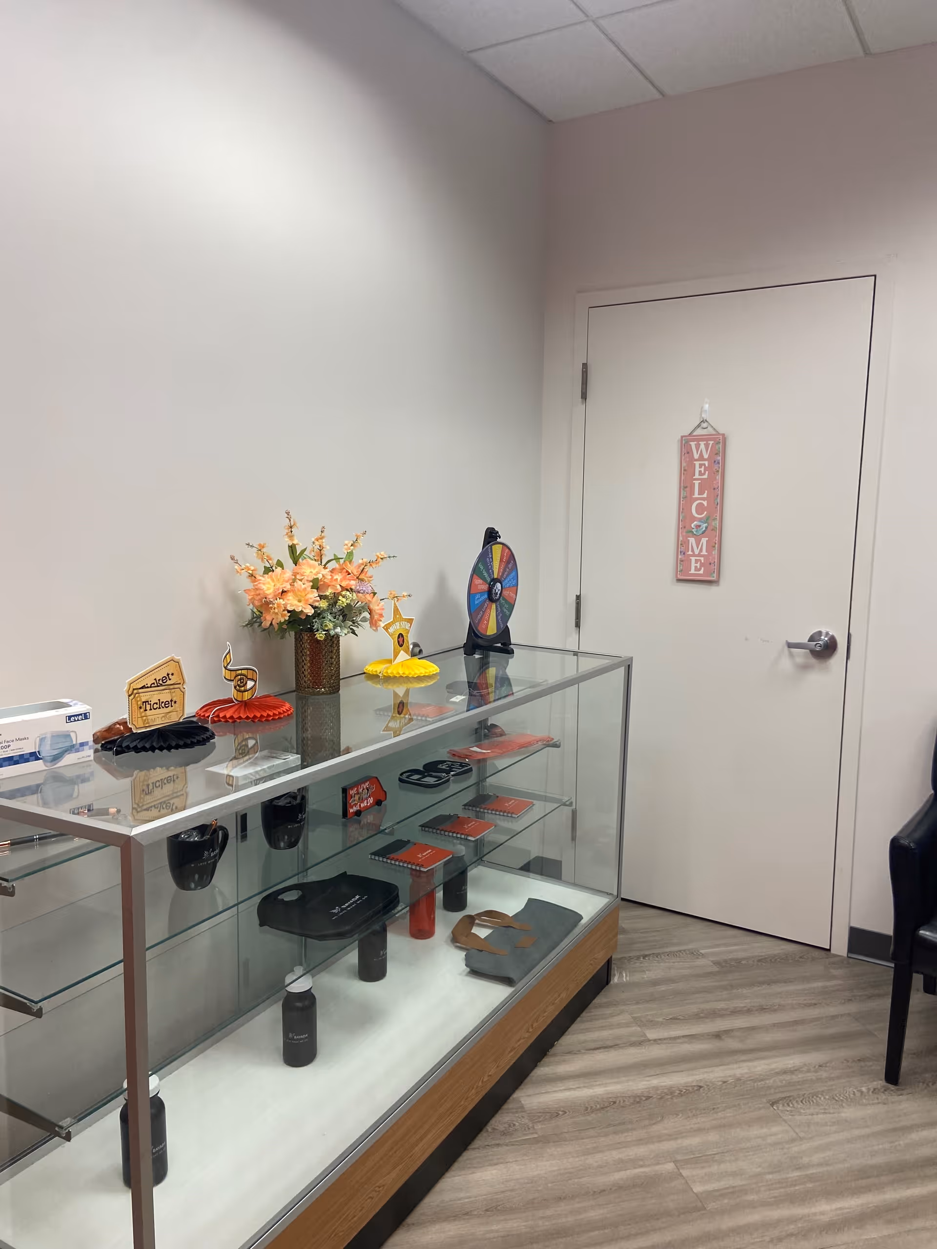 Glass display case with accessories and flowers in a reception hallway near a welcome door.