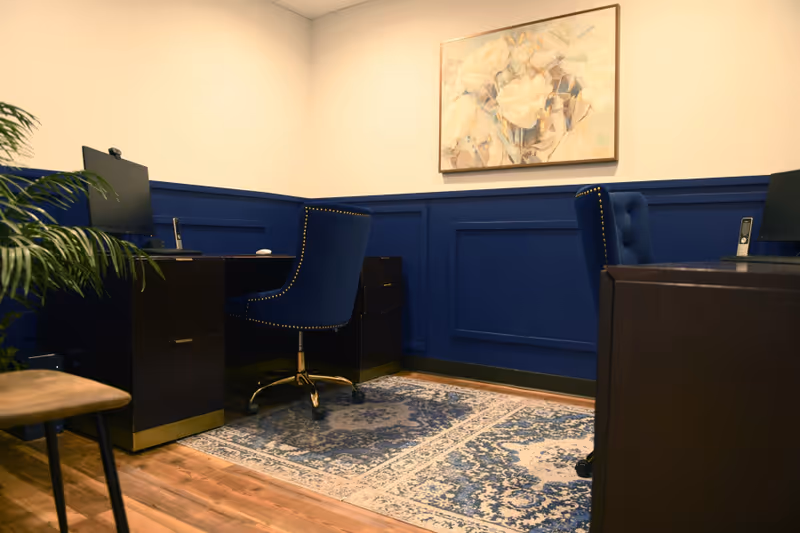 Blue-walled office area with desks, chairs, computers, and a decorative rug.