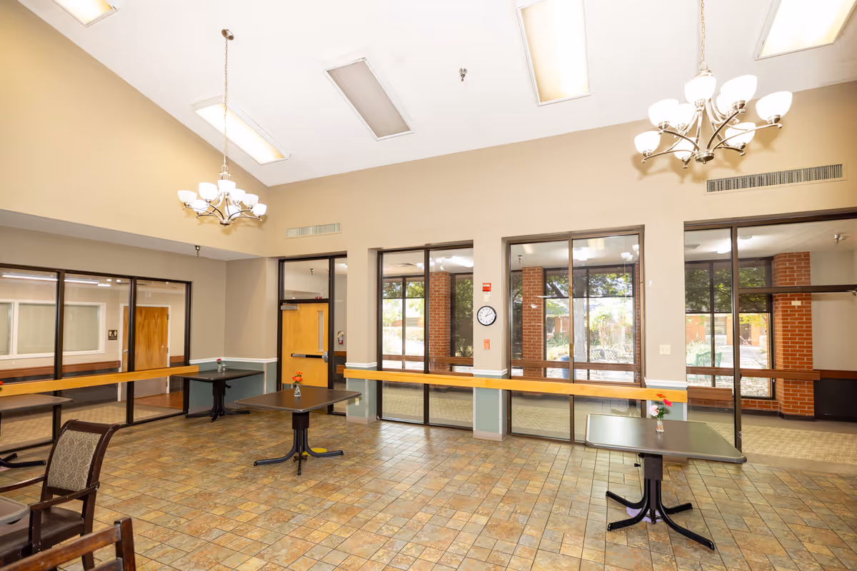 Bright interior dining/commons area with multiple tables, chandeliers, and glass doors.