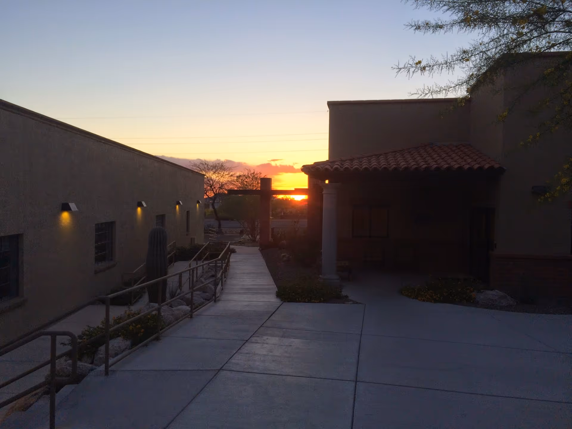 Sunset beyond the exterior of a hospice facility with walkways and desert landscaping.