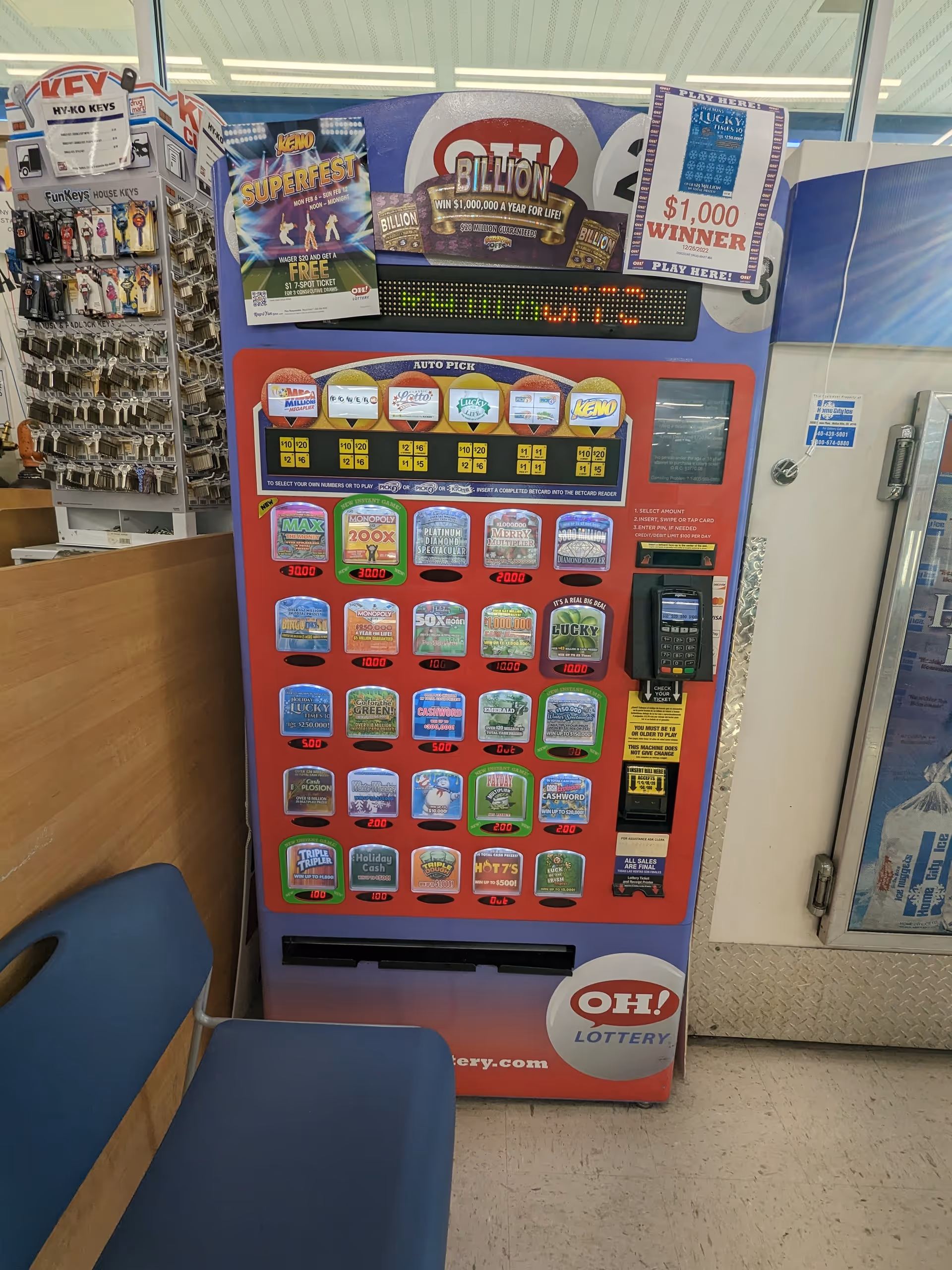 Inside a Discount Drug Mart, a red lottery vending machine stands beside seating and key rack.