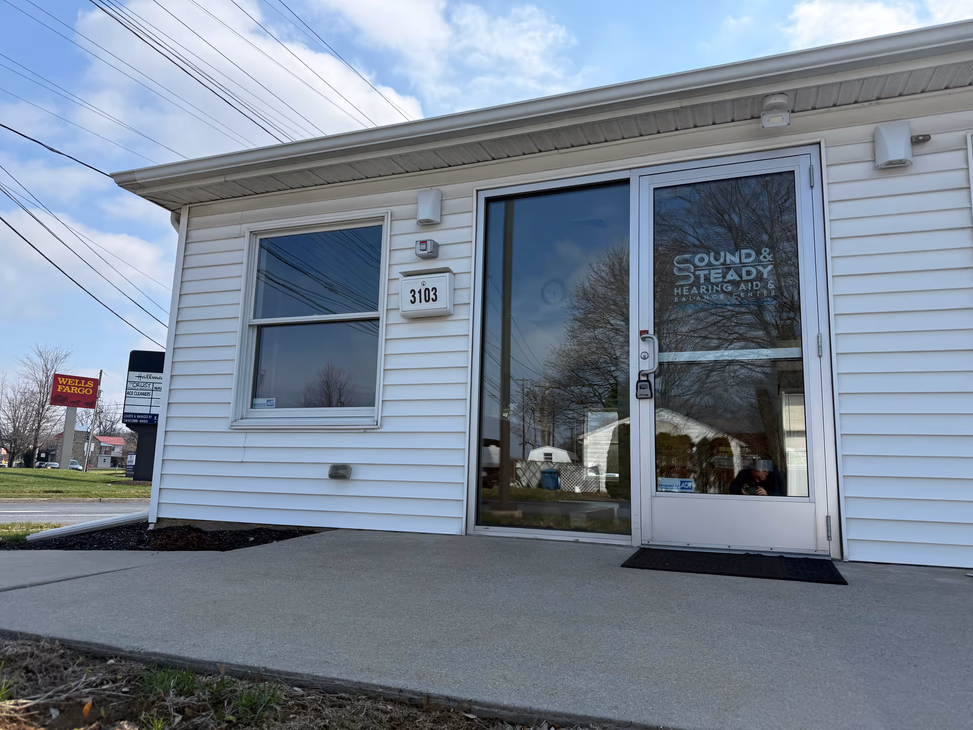 White office building entrance with glass door labeled Sound & Steady Hearing Aids.