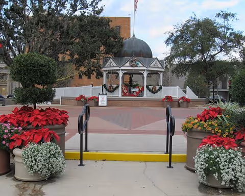 Outdoor courtyard with a white gazebo, red flowers in pots, and brick paving.