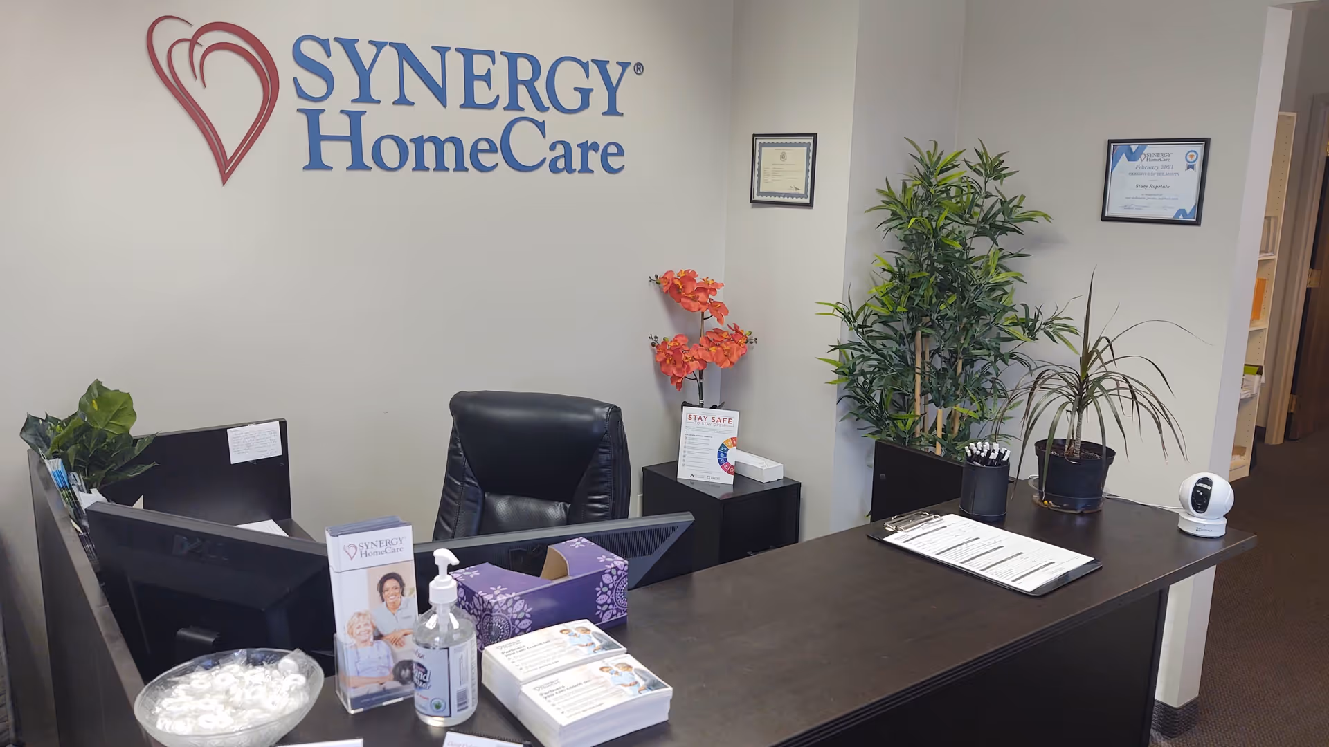 Reception area of SYNERGY HomeCare with desk, chair, plants, brochures.