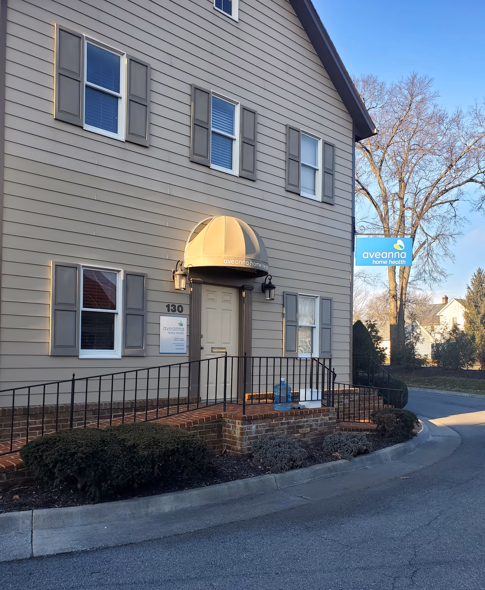Two-story gray facility with arched doorway awning and Aveanna Home Health sign in front