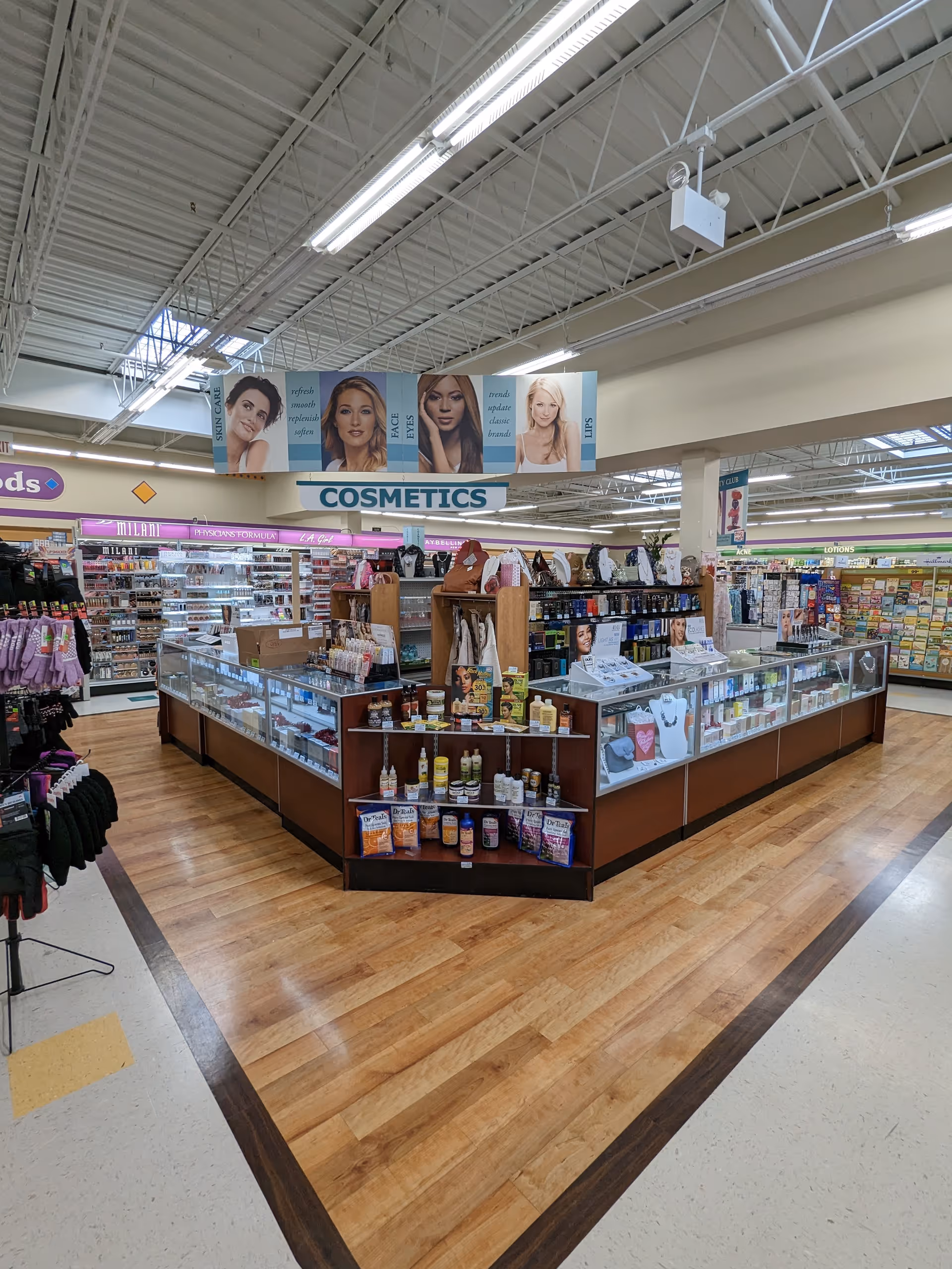 Inside a Discount Drug Mart store, a cosmetics counter displays products on wooden shelves.