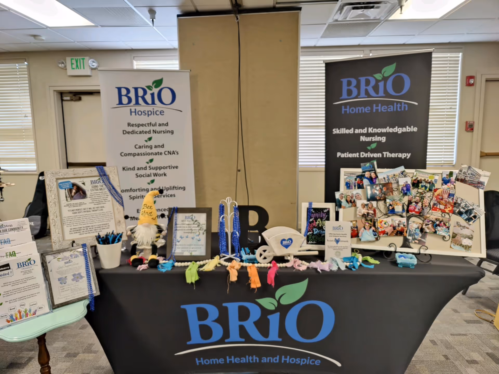 Display table with BRiO Hospice banners and photo boards in a bright interior room.