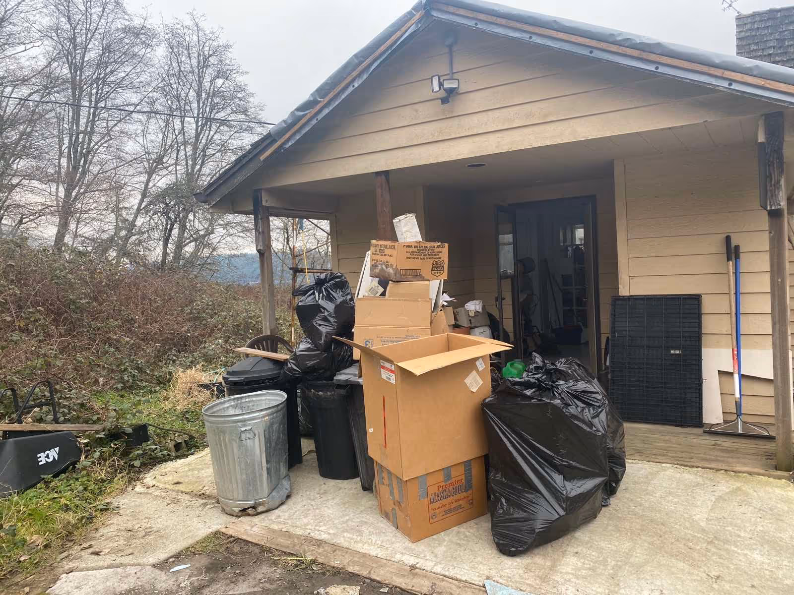 Front porch cluttered with trash bags and stacked cardboard boxes.