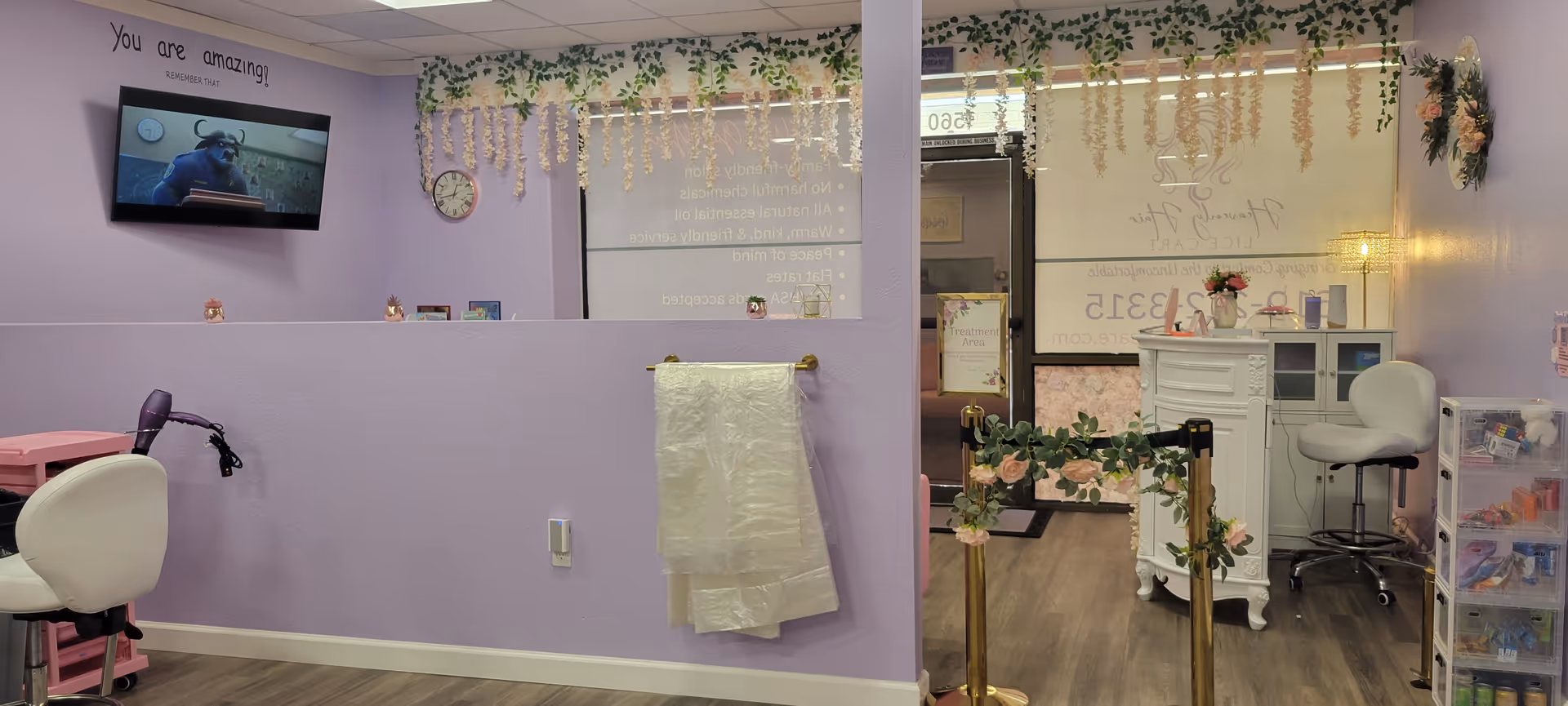 Lavender salon interior with styling chairs, reception area, hanging vines, and a wall-mounted TV.