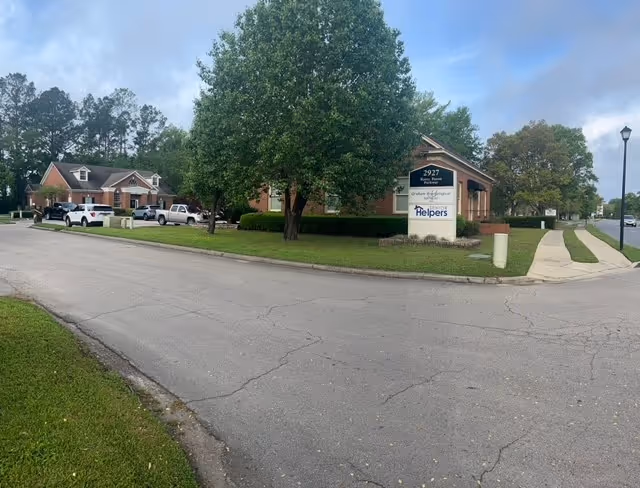 Exterior view of Senior Helpers facility with sign, trees, and a curved street.