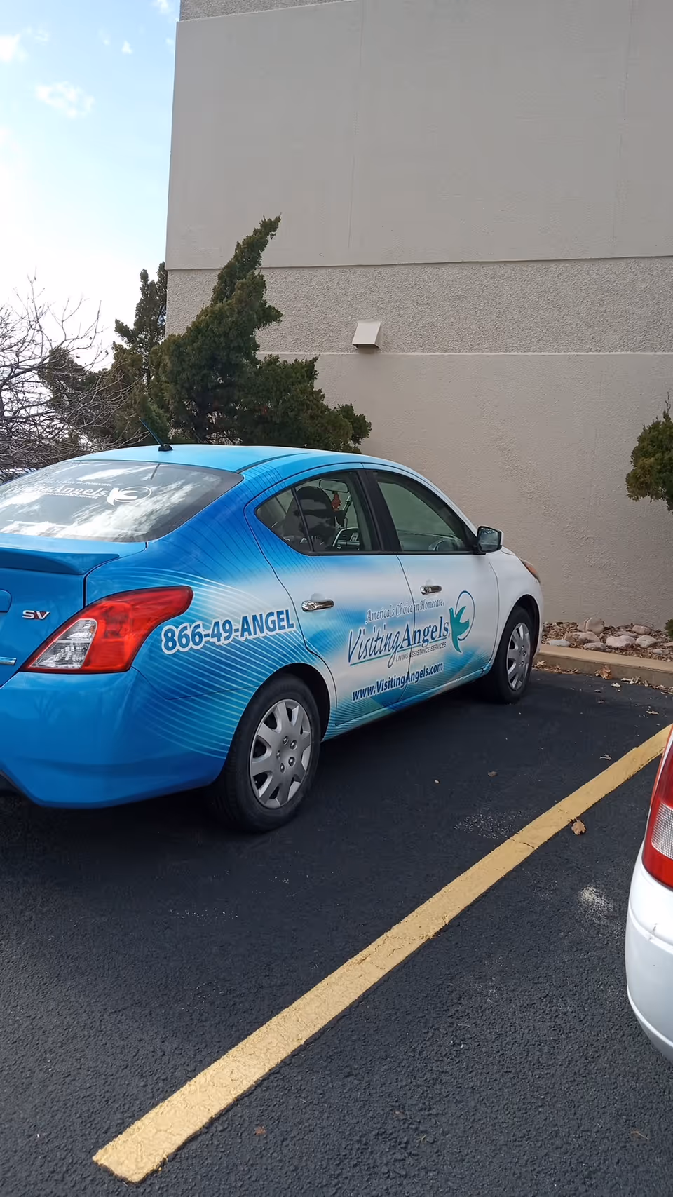 Blue Visiting Angels senior home care car parked in a parking lot beside a beige building.
