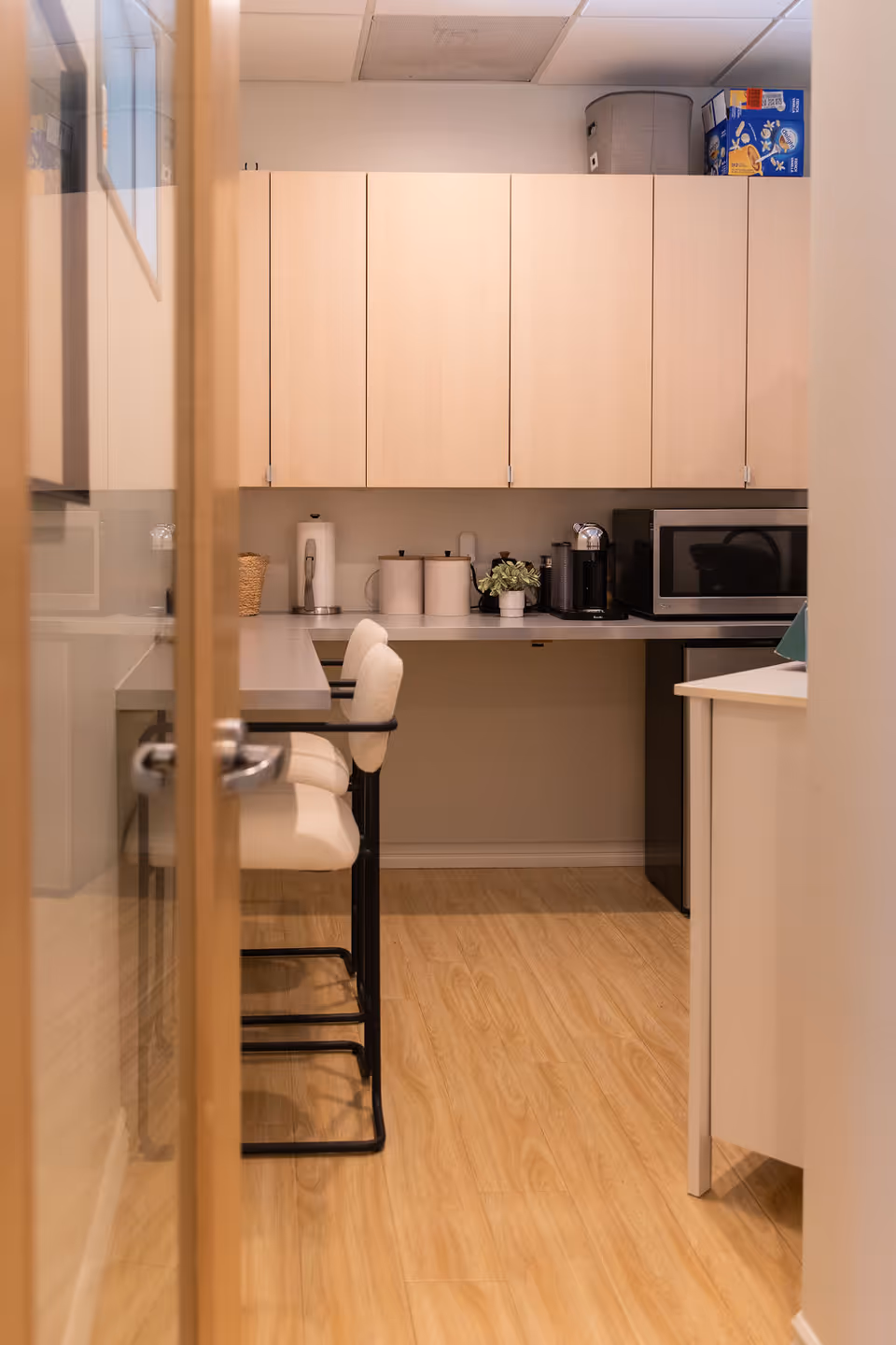Interior kitchenette in a senior facility with light cabinets, counter, bar stools, and appliances.