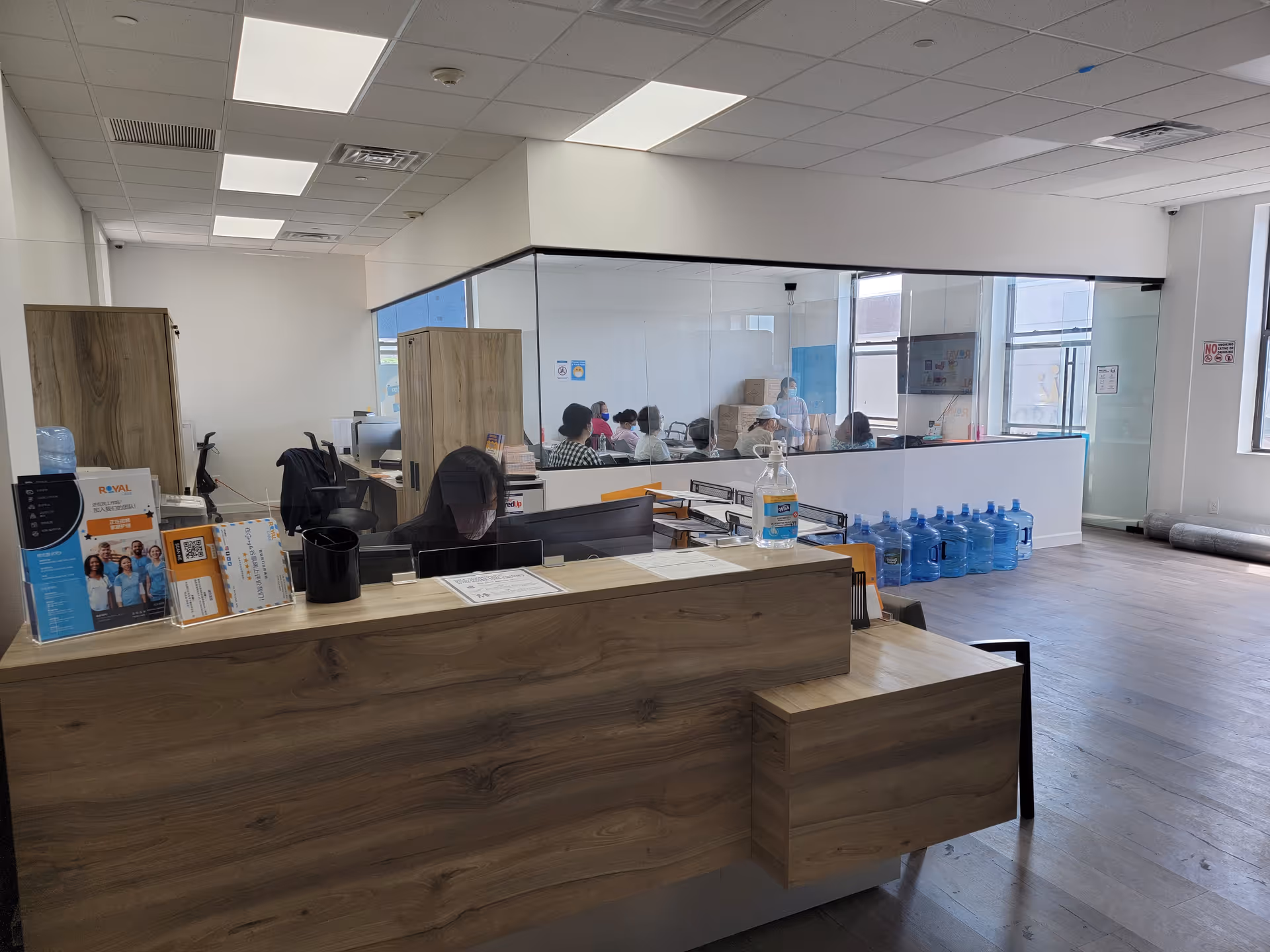 Reception desk in a modern senior living facility lobby with glass partition and water bottles.