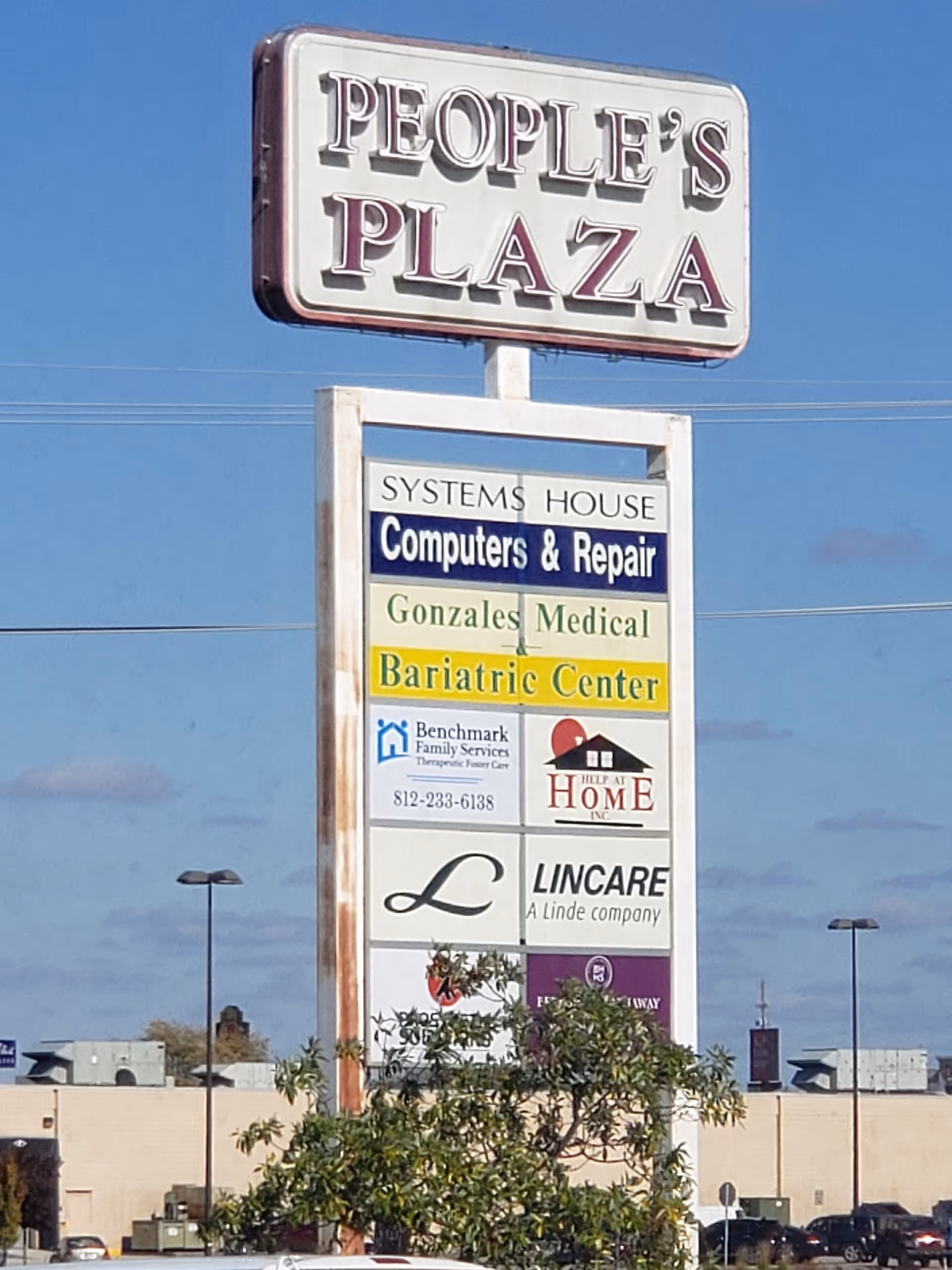 Tall outdoor signboard for People's Plaza with various business signs and blue sky.