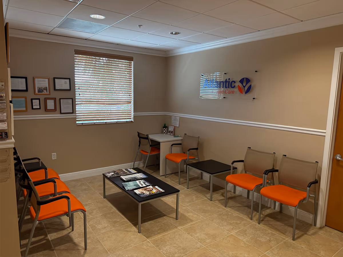 Beige-walled waiting area with orange-cushioned chairs, a coffee table, and a window.