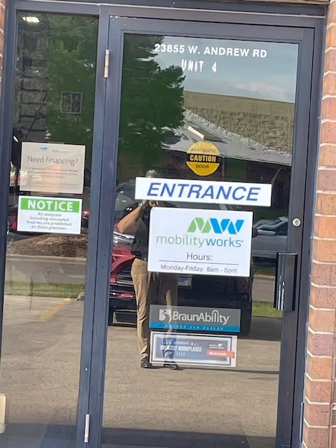 Glass entrance door of MobilityWorks with ENTRANCE sign and posted hours.