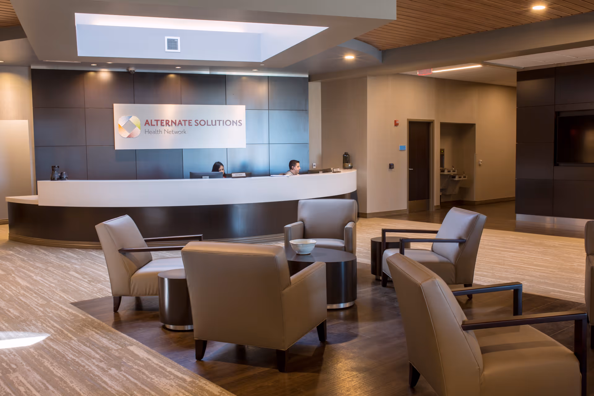 Modern senior living lobby with curved reception desk, staff, and comfortable lounge seating.