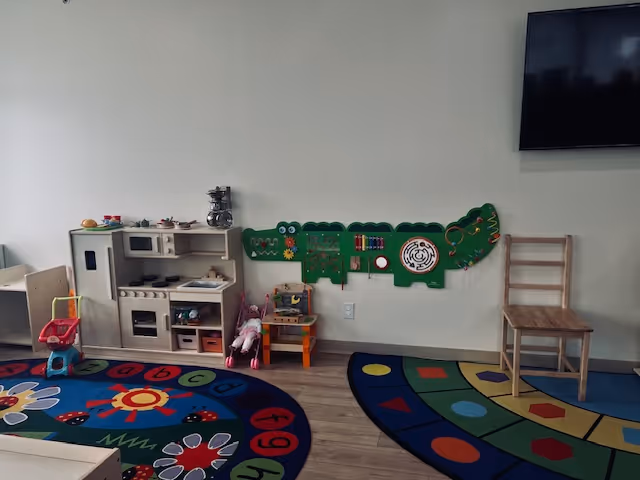 Indoor activity area featuring a toy kitchen, colorful rugs, and wall-mounted play panels.