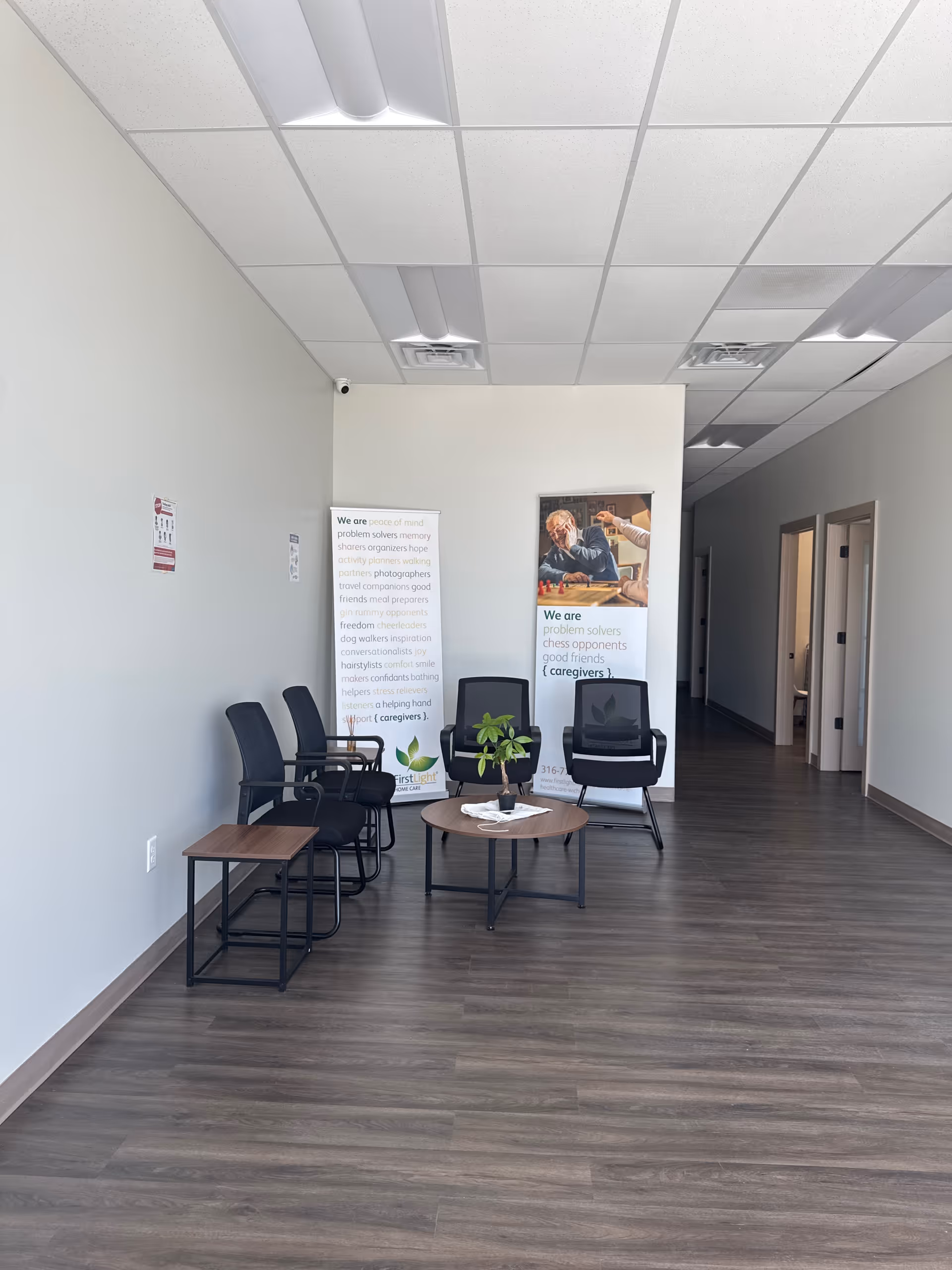 Waiting area inside a senior care facility with black chairs, a round table, and banners.