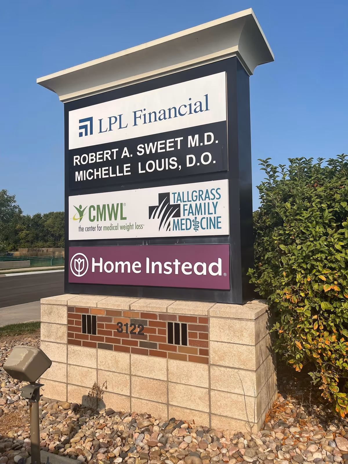 Tall outdoor sign displays Home Instead and partner logos beside a brick base
