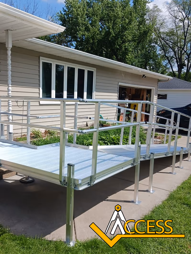 Metal wheelchair ramp along a residential exterior with beige siding and the Access logo.