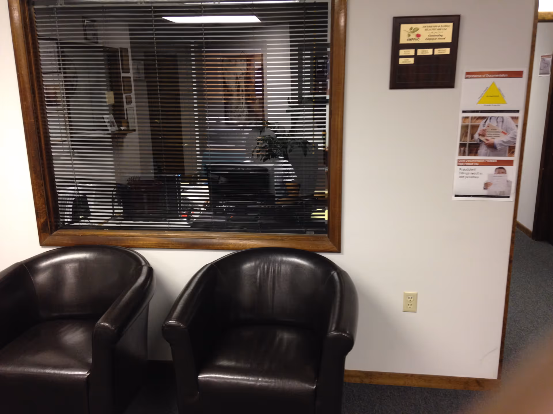 Lobby-style waiting area with two black leather chairs and a window with blinds.