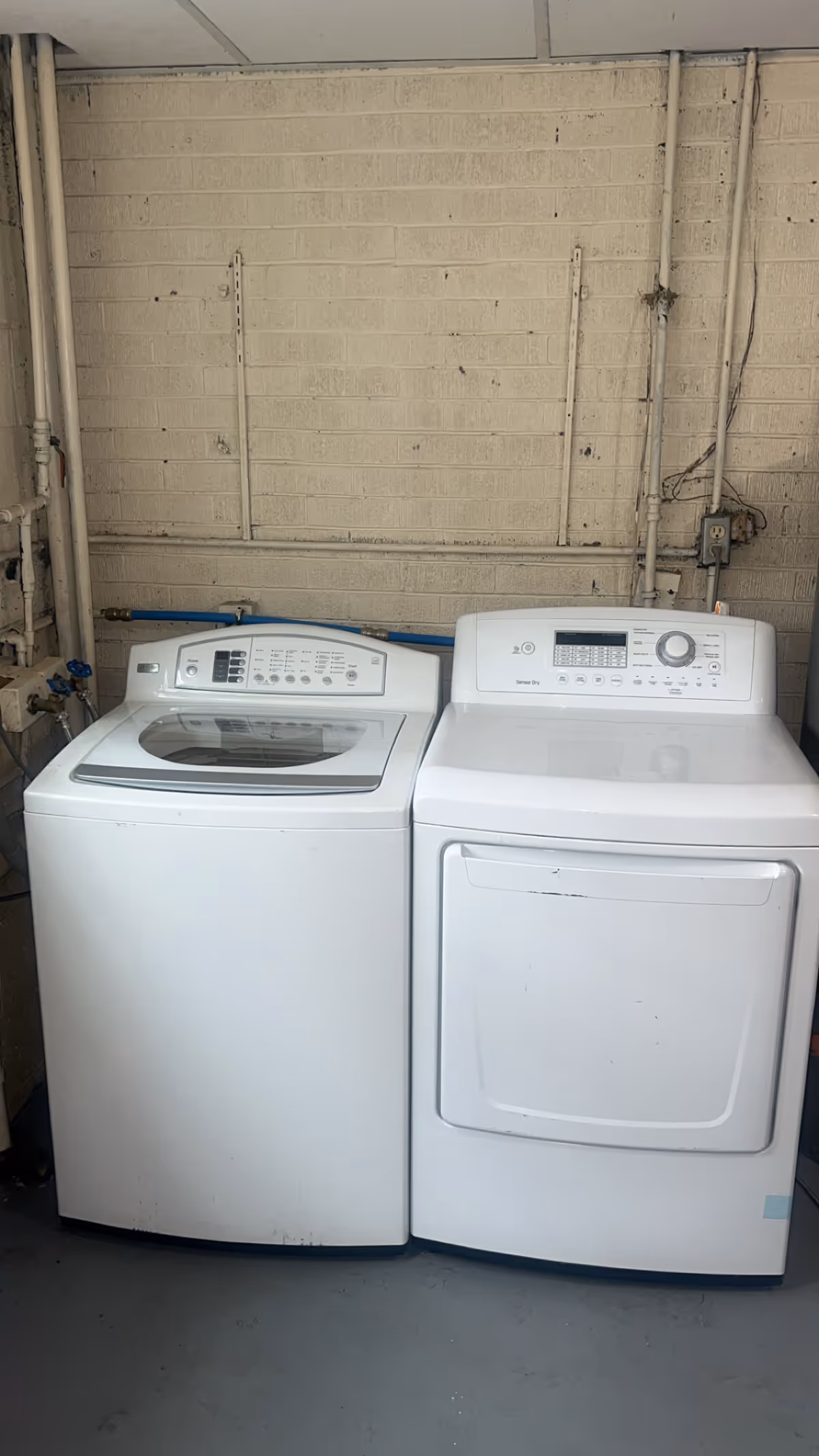 Laundry area with a washing machine and dryer against a brick utility wall in a basement.