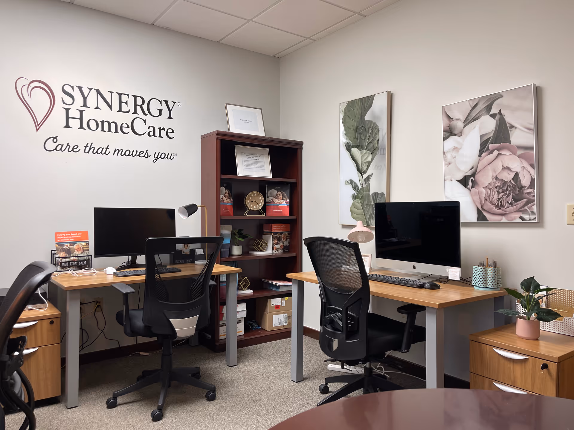 Office workspace inside a SYNERGY HomeCare facility with desks, computers, and wall art.