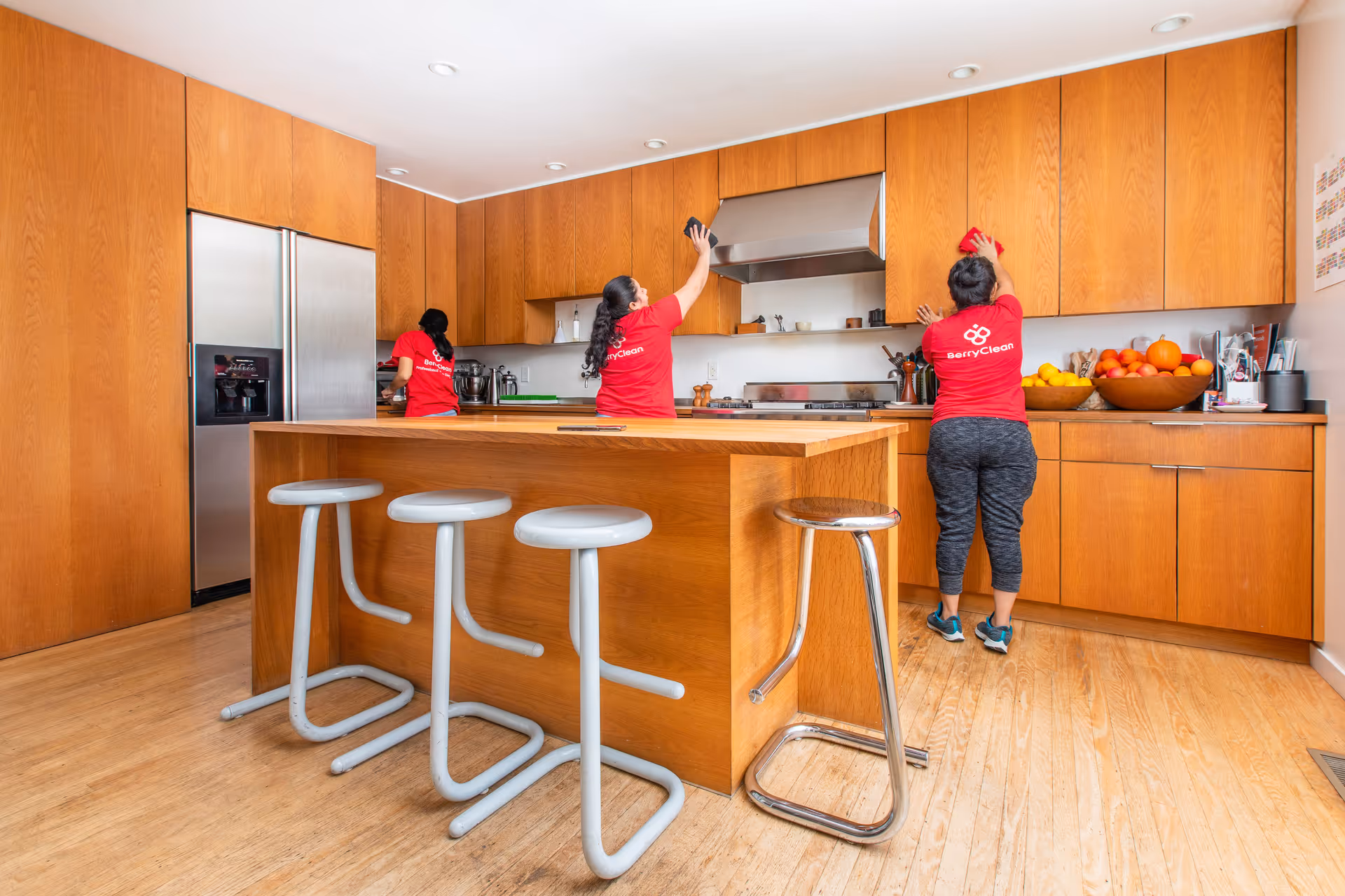 Three BerryClean staff in red shirts work in a modern wooden kitchen.