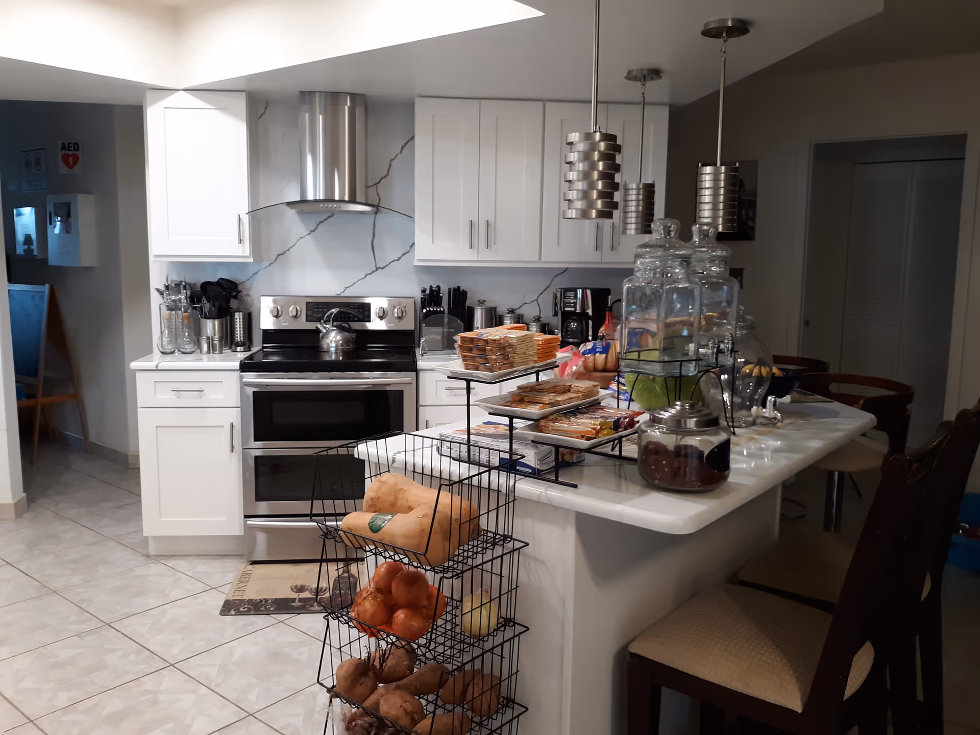 Bright white kitchen with stainless stove, marble backsplash, and a counter filled with snacks.