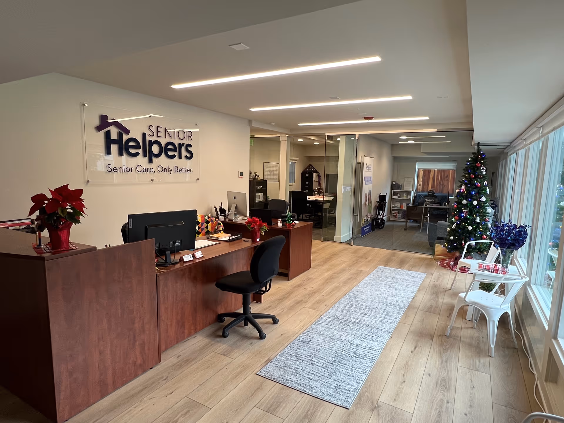 Reception area of Senior Helpers facility with sign, desks, chairs, Christmas tree, and large windows.